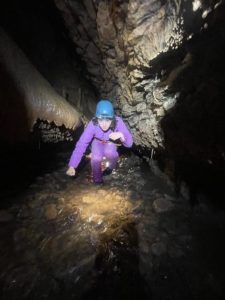 Une personne qui marche accroupie dans l'Aven des Côtes. Parcours spéléo aventure au coeur du massif calcaire du Sud Ardèche