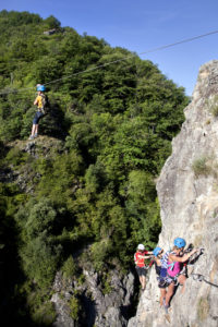 1 groupe de 4 personnes sur le Parcours Via Ferrata du Pont du Diable. Une participante sur une tyrolienne qui mène à l'autre rive de l'Ardèche. Les autres participants escalade pour rejoindre la tyrolienne.
